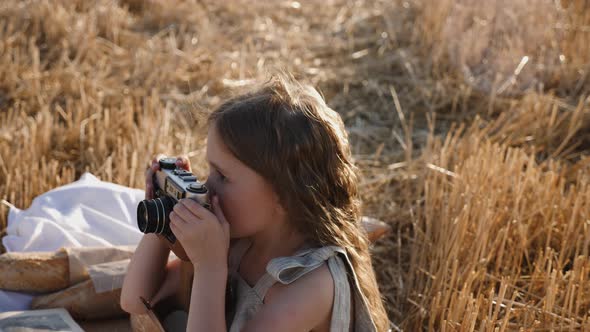 Serious Child Girl with Long Hair Sits on a Mown Wheat Field