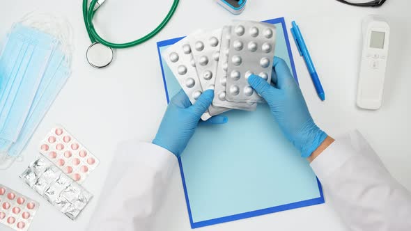 doctor in a white coat sits at the table and holds a stack of blister pills