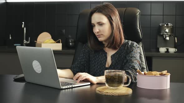 Young female typing on laptop keyboard and stretching during work on notebook at home