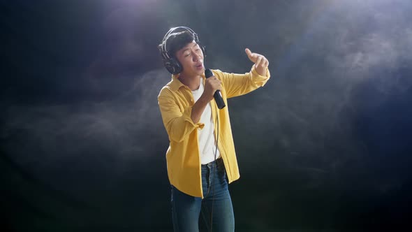 Asian Boy With Headphone Holding A Microphone And Rapping On The White Smoke Black Background