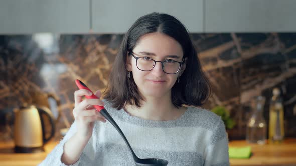Girl in Glasses Tasting the Deliciously Cooked Food From the Pot with a Ladle Looking at the Camera
