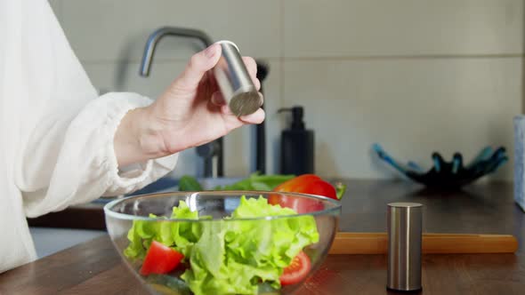 Woman Salting or Peppering Salad Before Dressing in Bowl Indoors