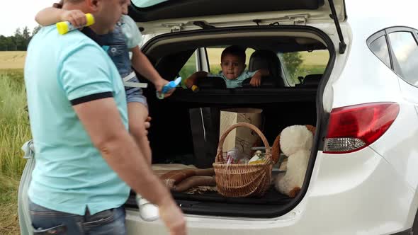 Couple with Kids Arrived at Picnic in Field By Car and Unload Luggage From Trunk in Slowmo