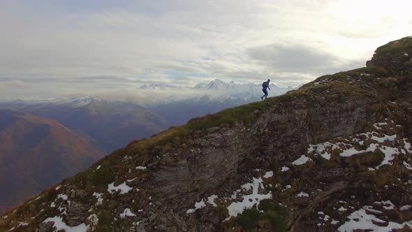 Aerial view of a trail runner running up the ridge of a snowy mountain.