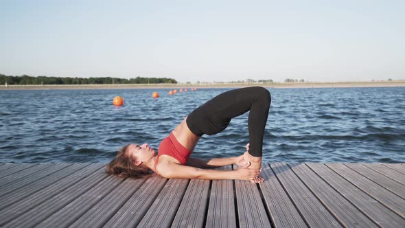Young athletic Caucasian girl in a red tank top and leggings is doing stretching and yoga
