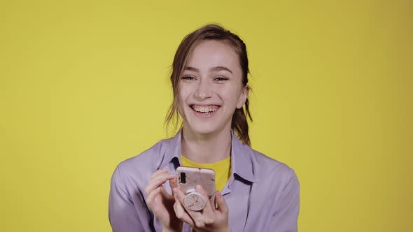 Smiling pensive young woman 20s makes an order via mobile phone sms in purple shirt posing