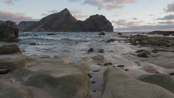 Low angle time lapse shot scenic beach at sunset light, Rocks in foreground