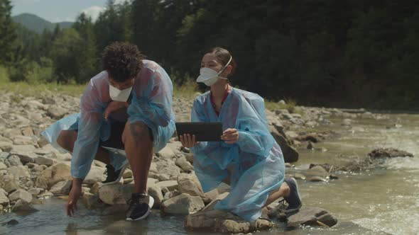 Professional Multiracial Ecologists with Tablet Pc Analyzing Water Contamination in Mountain River