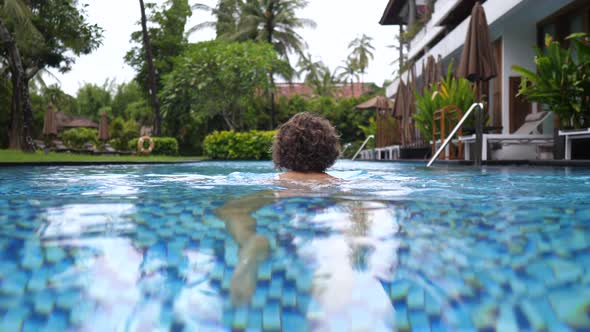 Camera Following Curly Lady Swimming in Her Private Pool