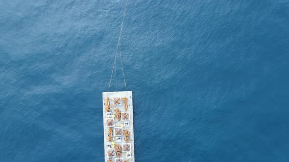 Floating barge with construction equipment being towed through the ocean by a tugboat. Drone view lo