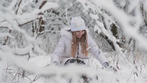 Portrait of a Teenage Girl Sitting in a Snowy Fairy Forest and Throwing Snow