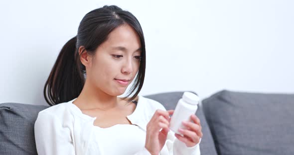 Woman checking ingredient on bottle of medicine at home