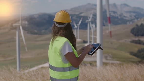 Woman engineer  in yellow hard hat and green uniform checking the wind turbine system