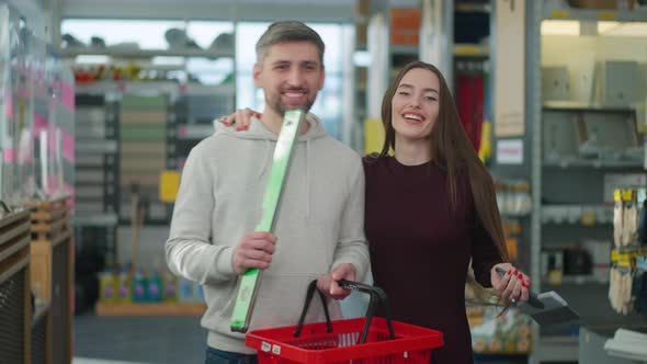 Cheerful Caucasian Couple Dancing and Singing Holding Shopping Basket and Tools