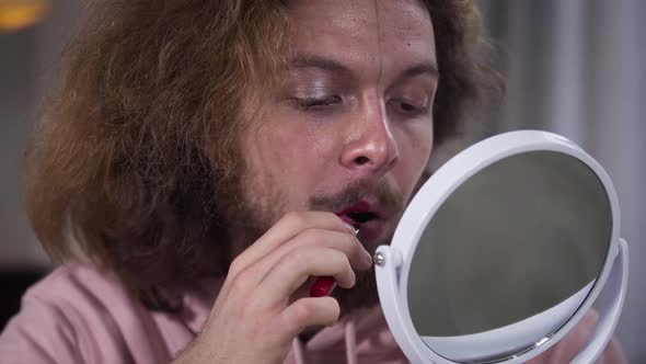 Close-up Portrait of Young Caucasian Man with Face Divided Into Two Parts Applying Red Lipstick