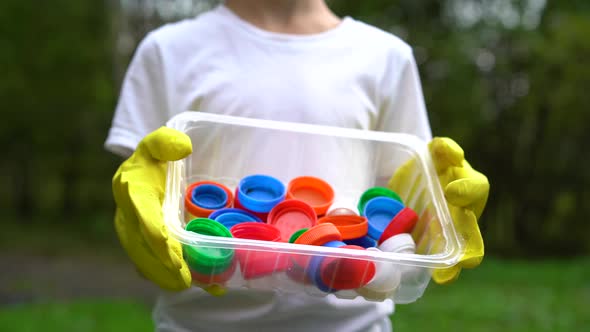 a Boy in the Park Holds Plastic Colored Lids in a Plastic Container the Concept of Proper Plastic