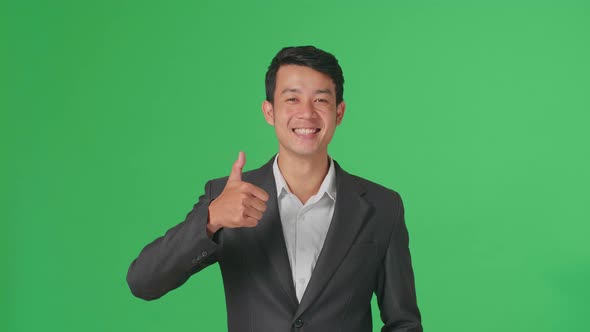 Happy Asian Business Man Showing Thumbs Up Gesture While Standing In The Green Screen Studio