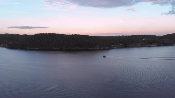 Drone pan of motorboat speeding along coastline during golden hour
