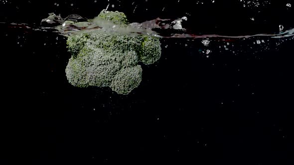 Colorful piece of broccoli being dropped into water in slow motion.