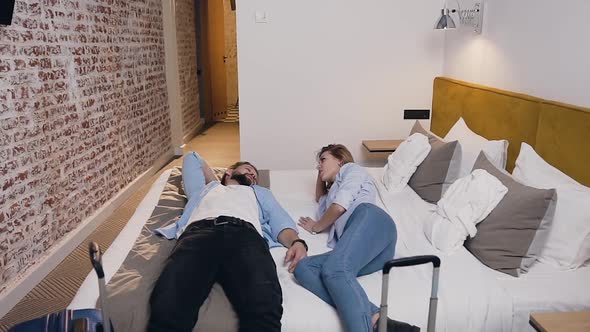 Happy Young Couple Lying on Bed in their Hotel Room and Talking