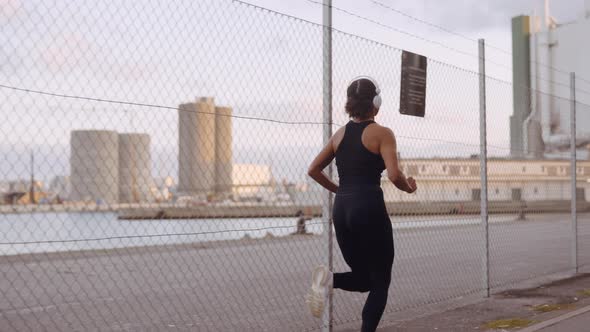 Young Woman In Sportswear And Headphones Running Along Harbour