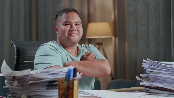 Close Up Of Fat Asian Man Crossing Arms And Smiling To Camera While Working With Documents