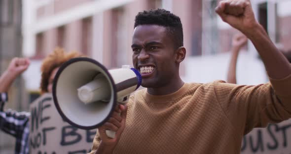 African american man shouting using megaphone with other people holding placards during protest
