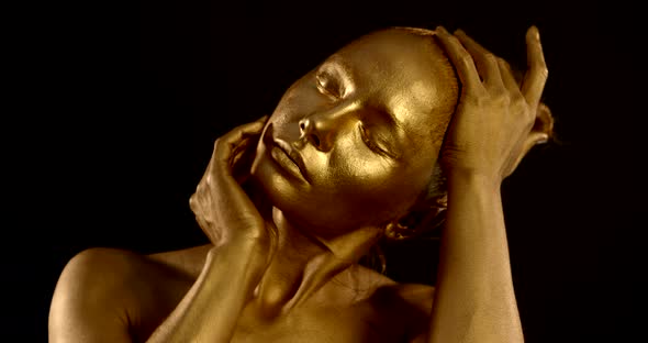 Close-up of a Woman's Head with Golden Glowing Skin on a Black Background. the Girl Strokes Her