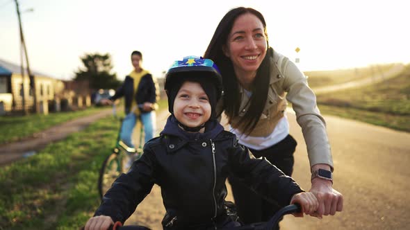 Front View Happy Face of Boy Riding a Bicycle While His Mother Runs Along Holding the Bike and