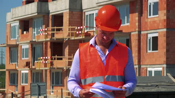 Construction Worker Studies Some Documents in Front of Building Site