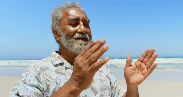 Front view of active senior African American man performing yoga on the beach 4k