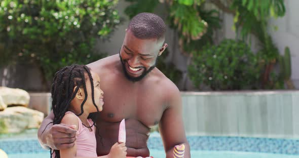 Happy african american father and daughter eating ice creams and embracing at swimming pool