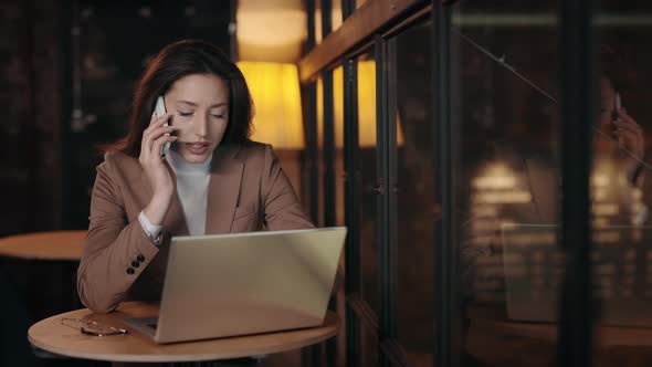 Young Woman Talking on Mobile Phone and Typing on Laptop