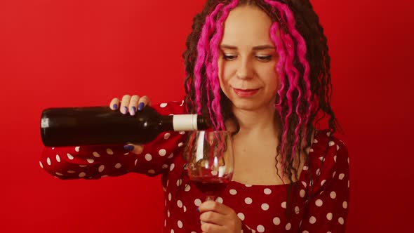 Young Woman Pours Red Wine Into Glass From Bottle on Red Background