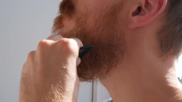 Adult man cutting his own beard and mustache with scissors comb Caucasian red bearded male face 4K