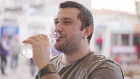 Young man drinking water from pet bottle on city background smiling and feeling good