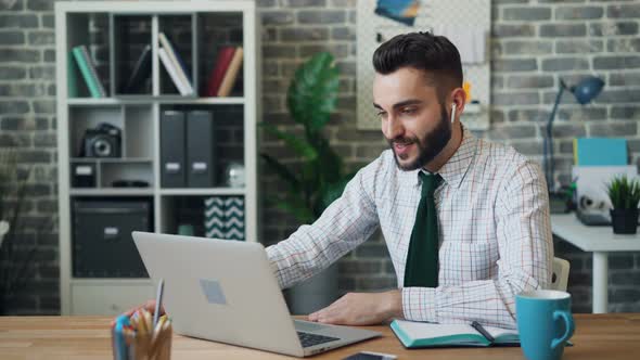 Joyful Office Worker Making Video Call with Laptop Wireless Earphones at Work