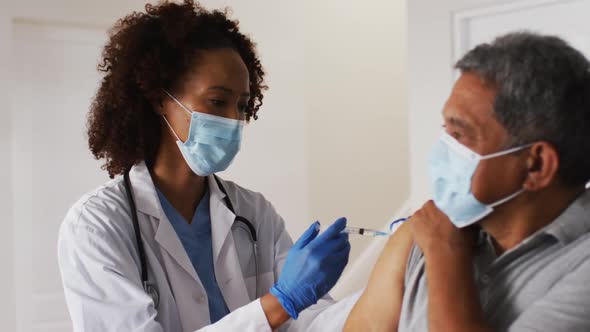 Mixed race female doctor wearing mask giving vaccination to senior man at home