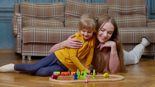 Mother Playing with Child Kid Daughter Riding Toy Train on Wooden Railroad Blocks Board Game at Home