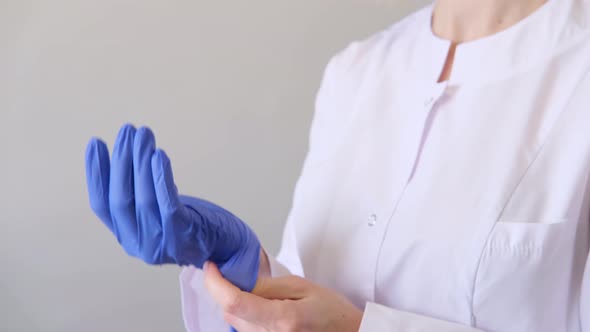 A Female Doctor Surgeon in White Uniform Puts on Blue Gloves