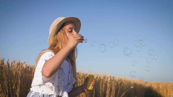 Little Girl Blowing Soap Bubbles in Wheat Field at Sunset Time. Slow Motion Video.