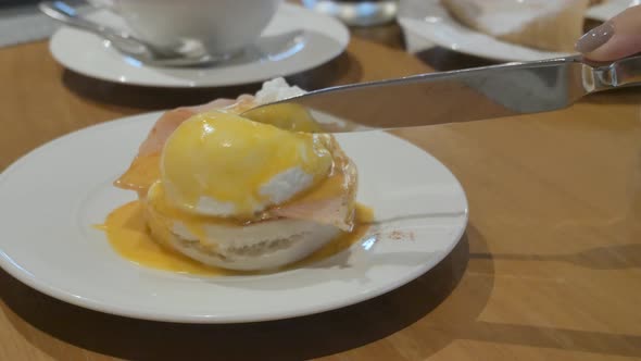hand of woman cutting fresh egg benedict poached egg for breakfast
