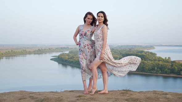 Pretty Barefoot Women in Dresses Pose on Hill Against River