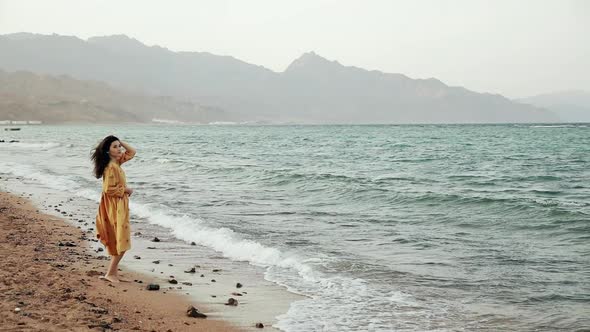 Attractive Brunette Woman Walking on a Deserted Beach at Windy Weather. Gorgeous Slim Mixed Race