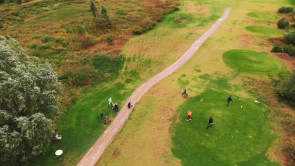 Aerial Drone View of a Couple of Golf Players Standing Near a Narrow Dirt Street on a Grassy Golf