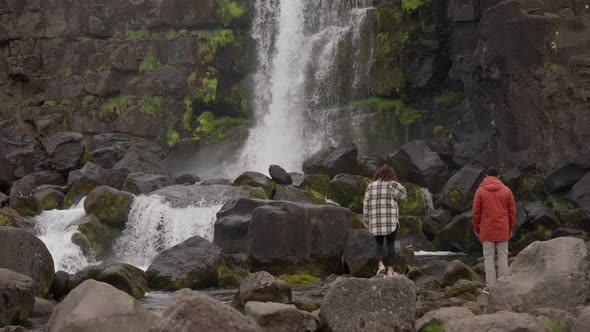 Couple Standing On Rocks By Oxararfoss Waterfall