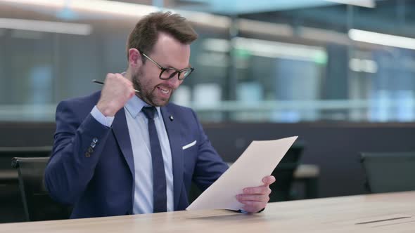 Middle Aged Businessman Celebrating Success While Reading Documents