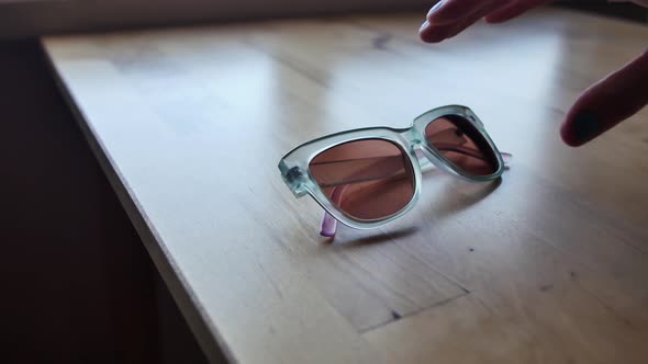 Cat-eye sunglasses are picked up off light wood table by a hand