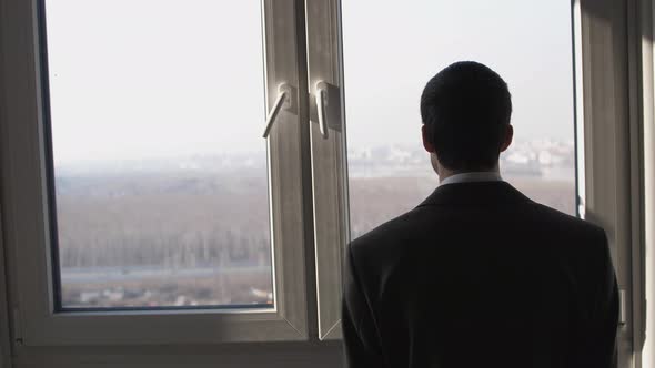 Young Successful Businessman Standing in Front of Windows Looking Into Distance on the City