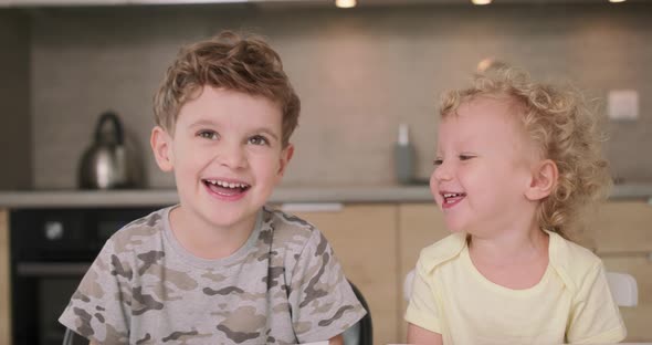 Adorable Brother and Sister Smile and Laugh Together While Sitting at the Kitchen Table